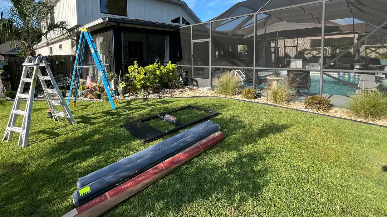 Ladders, a replacement screen door frame and rolls of new screen laid out on the lawn before a pool cage rescreening