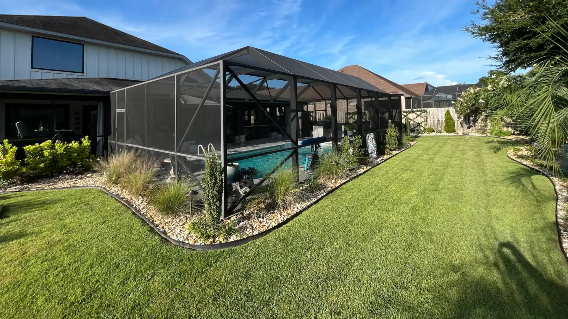 Newly rescreened black pool cage enclosure behind a two-story home