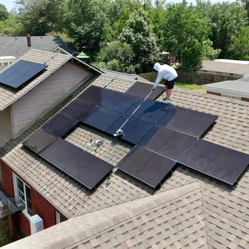 Drone view of a crew member cleaning a rooftop solar array on a two-story brick home