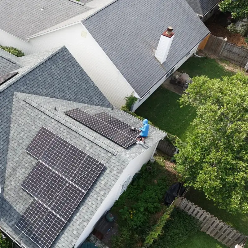 Aerial view of a gray shingle roof with several solar arrays, a crew member cleaning the panels on the back slope